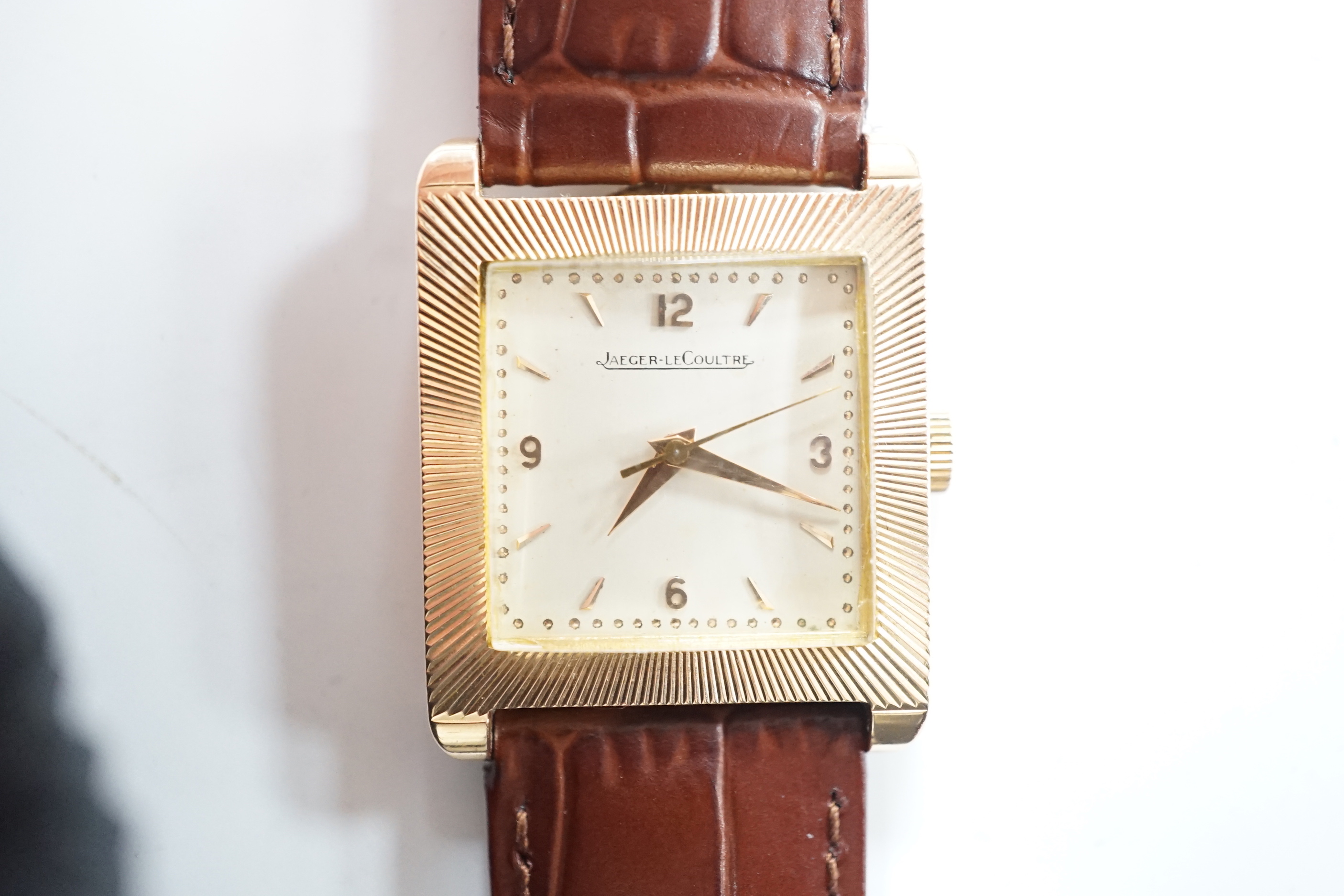 A gentleman's 18ct gold Jaeger LeCoultre manual wind dress wrist watch, with square dial, milled bezel and baton and quarterly Arabic numerals, on associated leather strap, case diameter 26mm, gross weight 31.8 grams.
